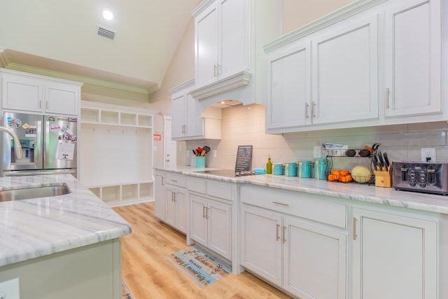 kitchen featuring stainless steel fridge, light hardwood / wood-style flooring, white cabinetry, tasteful backsplash, and light stone countertops