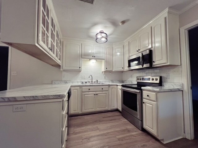 kitchen with sink, stainless steel appliances, decorative backsplash, white cabinets, and light wood-type flooring