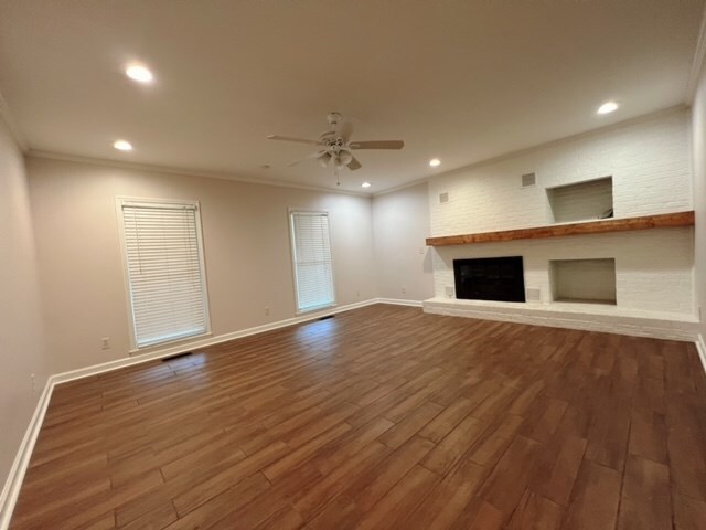 unfurnished living room with ceiling fan, wood-type flooring, ornamental molding, and a brick fireplace