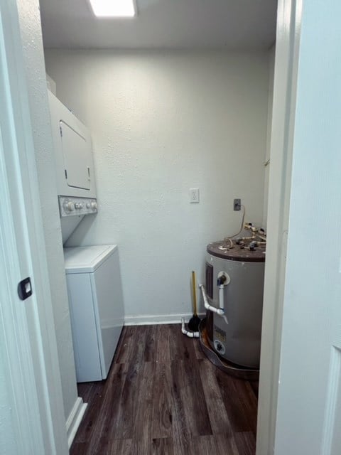 washroom with dark hardwood / wood-style flooring, stacked washer / drying machine, and water heater