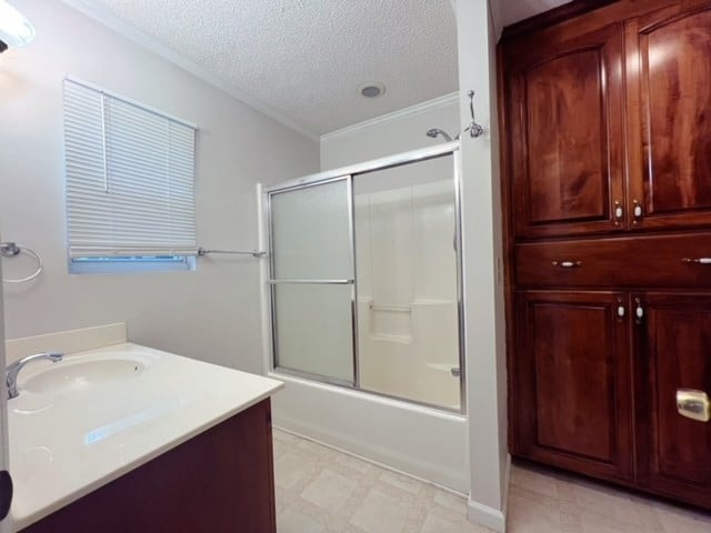 bathroom featuring vanity, crown molding, shower / bath combination with glass door, and a textured ceiling