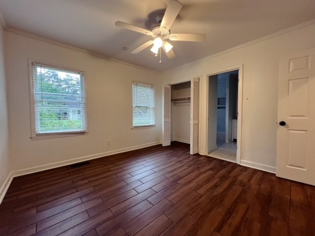 unfurnished bedroom with crown molding, ceiling fan, and dark wood-type flooring