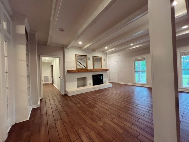 unfurnished living room with beamed ceiling, dark hardwood / wood-style floors, and a fireplace