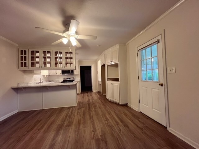 kitchen featuring dark wood-type flooring, white cabinets, ornamental molding, kitchen peninsula, and stainless steel appliances