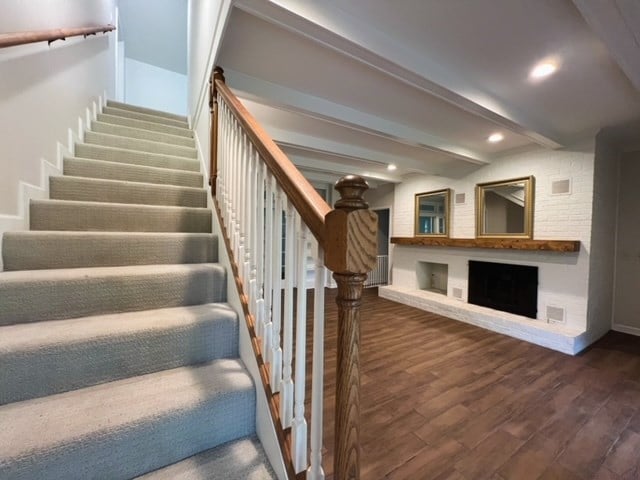 stairs with hardwood / wood-style flooring, beam ceiling, and a fireplace