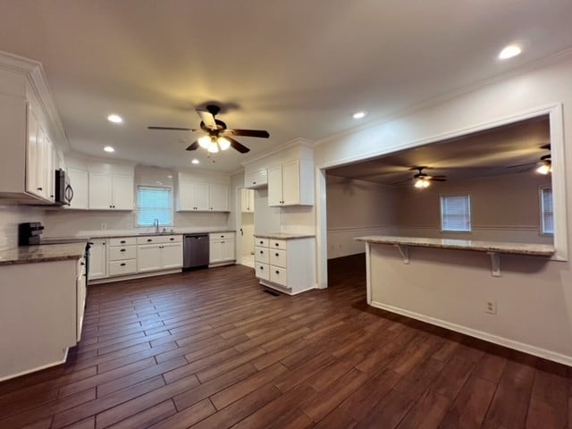 kitchen with white cabinetry, dark hardwood / wood-style flooring, crown molding, a breakfast bar, and appliances with stainless steel finishes