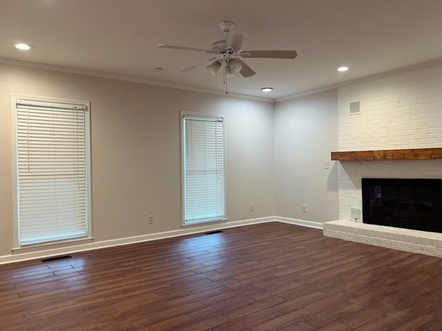 unfurnished living room featuring a fireplace, crown molding, ceiling fan, and dark wood-type flooring