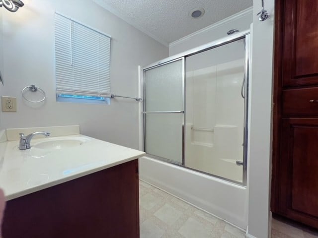 bathroom featuring shower / bath combination with glass door, crown molding, vanity, and a textured ceiling