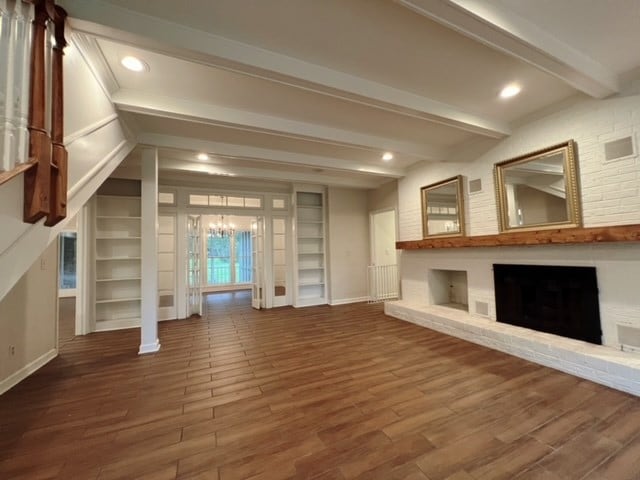 unfurnished living room featuring hardwood / wood-style floors, an inviting chandelier, beamed ceiling, and a brick fireplace