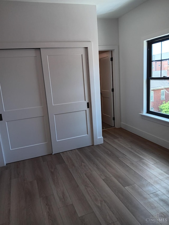 unfurnished bedroom featuring wood finished floors, a closet, and baseboards