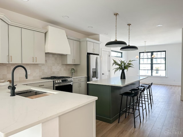 kitchen with appliances with stainless steel finishes, a sink, a center island, custom range hood, and a breakfast bar area