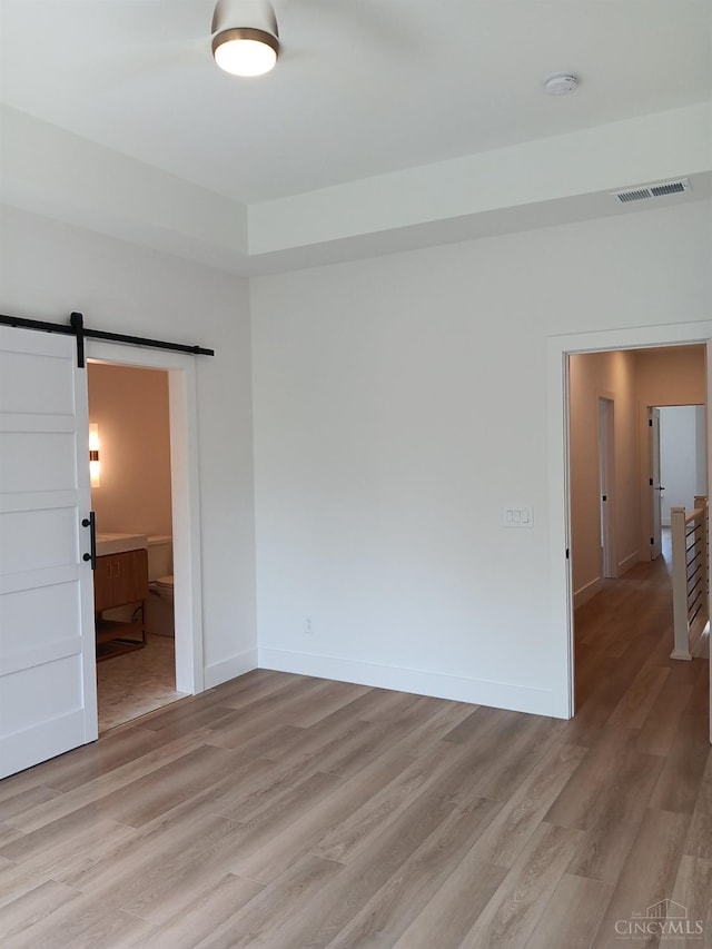 unfurnished room with a barn door, light wood-type flooring, a smoke detector, and baseboards