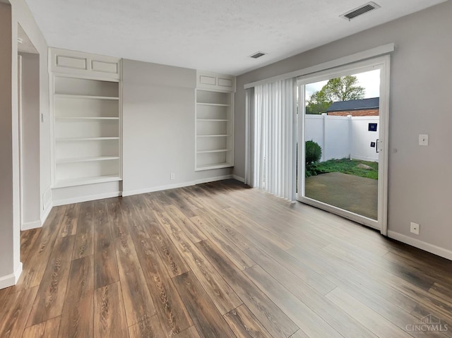 unfurnished living room with built in shelves, dark wood-type flooring, and a textured ceiling