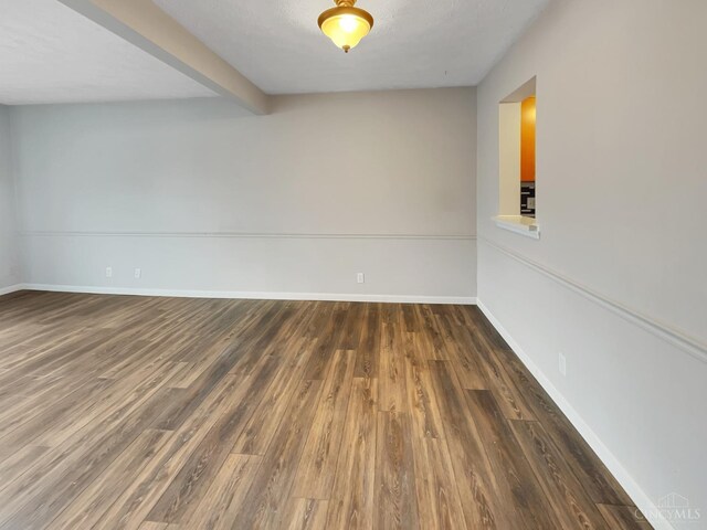 unfurnished room with dark hardwood / wood-style floors and beamed ceiling