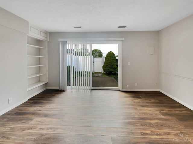 unfurnished room featuring built in shelves and dark hardwood / wood-style floors