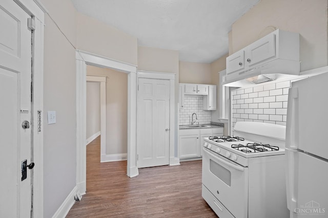 kitchen featuring white appliances, a sink, white cabinetry, decorative backsplash, and wood finished floors