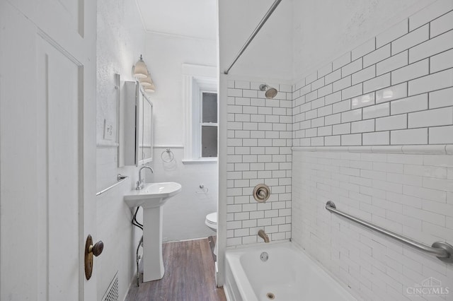 bathroom with toilet, wood finished floors, shower / tub combination, and tile walls