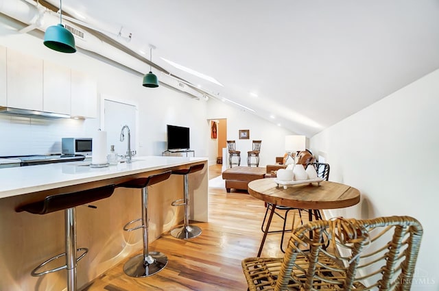 kitchen featuring lofted ceiling, white cabinets, hanging light fixtures, light hardwood / wood-style flooring, and tasteful backsplash