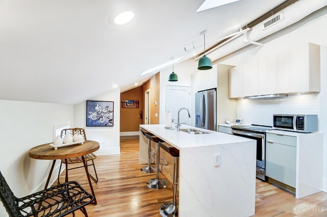 kitchen with light hardwood / wood-style floors, decorative light fixtures, a center island with sink, white cabinets, and appliances with stainless steel finishes