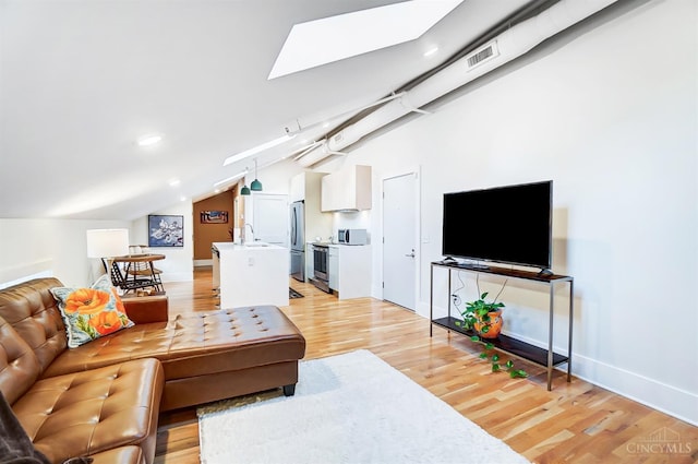 living room with light hardwood / wood-style floors, lofted ceiling with skylight, and sink