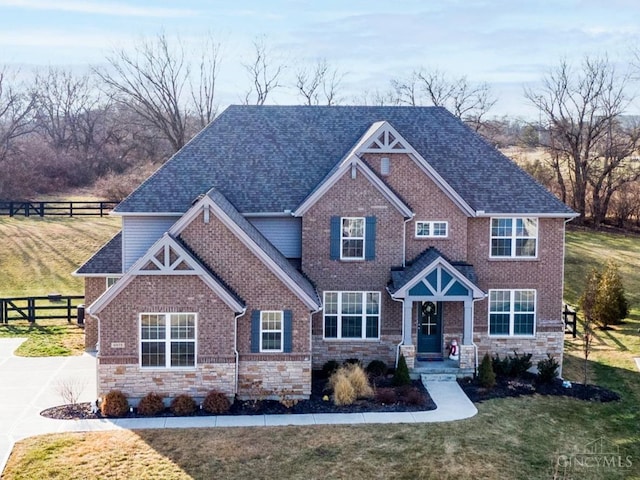 craftsman house featuring stone siding, a front lawn, and fence