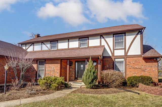 tudor home featuring brick siding, a chimney, a front yard, and stucco siding
