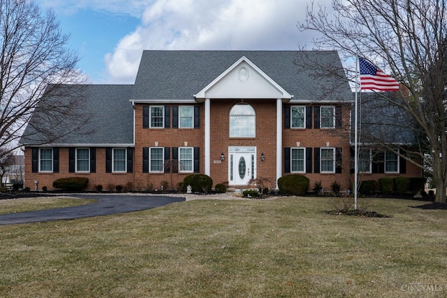 greek revival house with a front lawn, a shingled roof, and brick siding