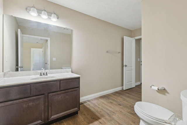 bathroom featuring baseboards, toilet, wood finished floors, a textured ceiling, and vanity