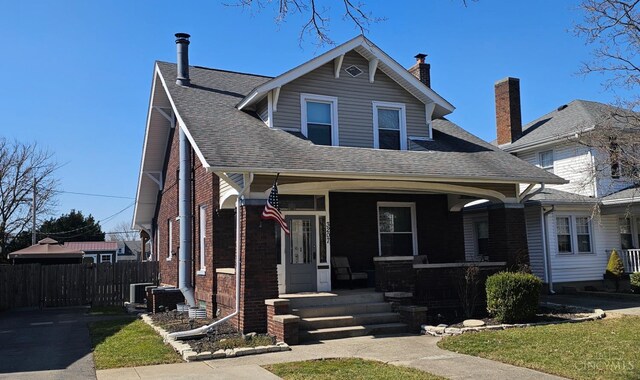 view of front of house with a porch, a shingled roof, and fence