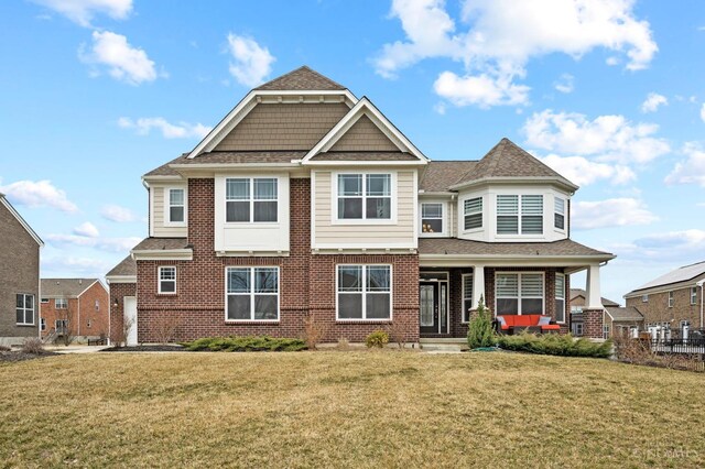 view of front facade featuring brick siding, a front yard, and a shingled roof