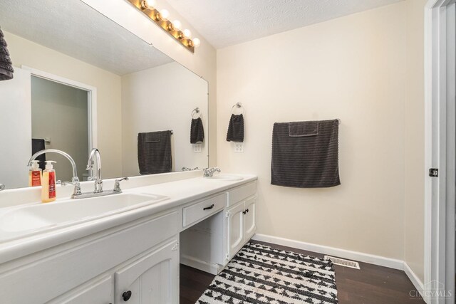 bathroom featuring baseboards, wood finished floors, double vanity, and a textured ceiling