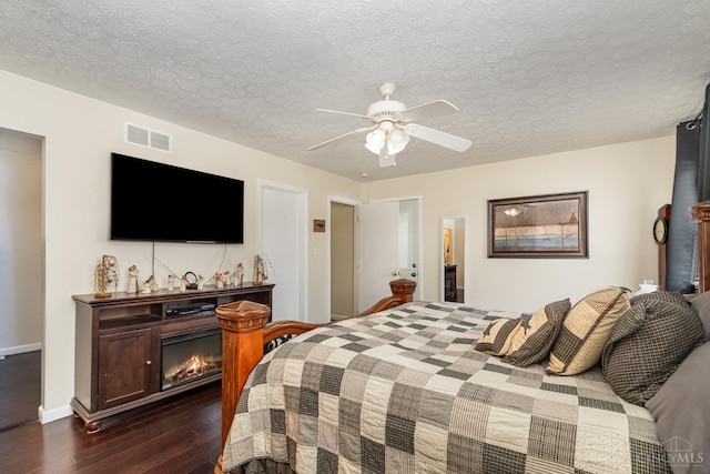 bedroom with dark wood-style floors, a glass covered fireplace, a ceiling fan, baseboards, and a textured ceiling