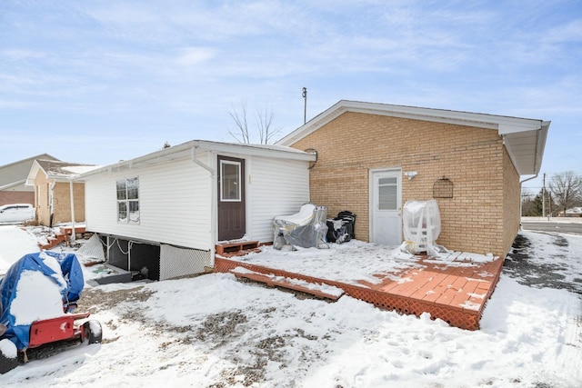 snow covered property featuring brick siding, a deck, and a garage