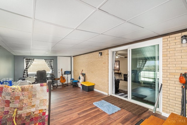 interior space featuring brick wall, wood finished floors, a drop ceiling, baseboards, and a ceiling fan