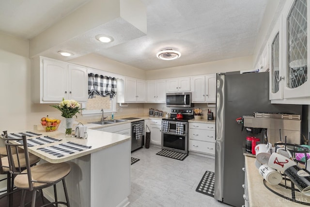 kitchen with appliances with stainless steel finishes, a sink, a peninsula, white cabinetry, and a textured ceiling