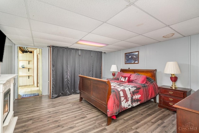 bedroom with wood finished floors, a drop ceiling, and a decorative wall