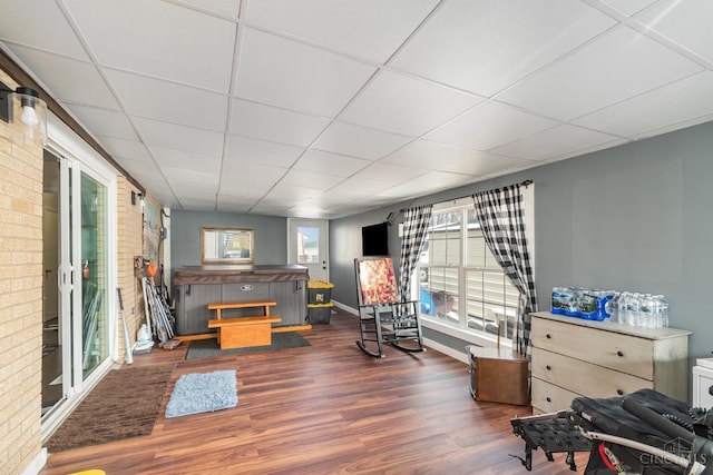 living area featuring dark wood finished floors, a drop ceiling, brick wall, and baseboards