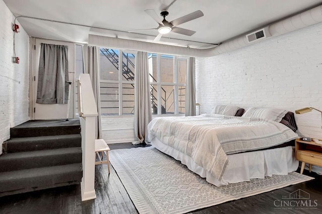 bedroom featuring a ceiling fan, visible vents, brick wall, and wood finished floors