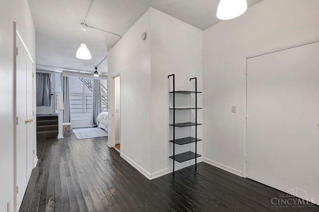 corridor featuring stairs, dark wood-type flooring, and baseboards
