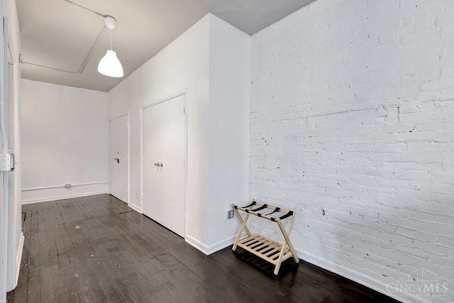 hallway featuring brick wall, baseboards, and dark wood-type flooring