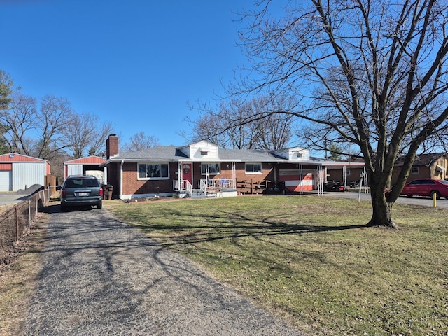 ranch-style home featuring driveway, an outdoor structure, a front yard, brick siding, and a chimney