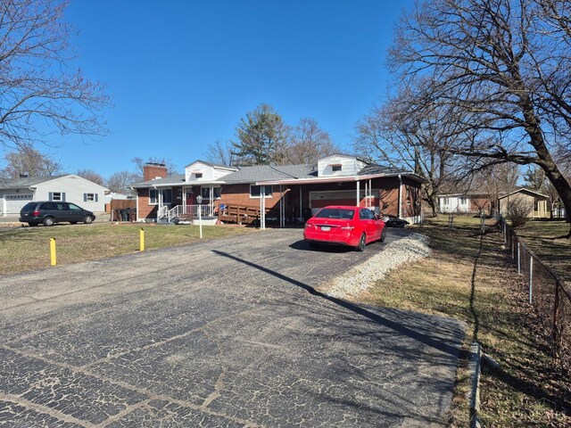 view of front of property featuring fence, a chimney, a front lawn, aphalt driveway, and brick siding