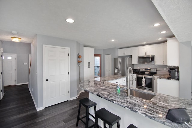 kitchen with a sink, stainless steel appliances, dark stone counters, and white cabinetry