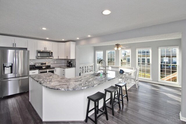 kitchen featuring light stone countertops, a sink, white cabinets, appliances with stainless steel finishes, and backsplash