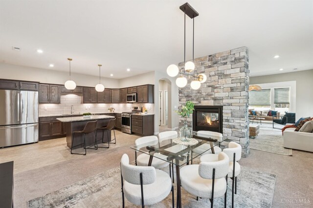 dining room featuring arched walkways, a stone fireplace, and recessed lighting