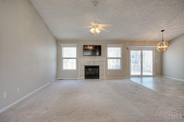 unfurnished living room with baseboards, a fireplace, a textured ceiling, light carpet, and ceiling fan with notable chandelier