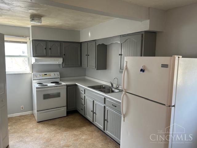 kitchen with gray cabinetry, under cabinet range hood, light countertops, white appliances, and a sink