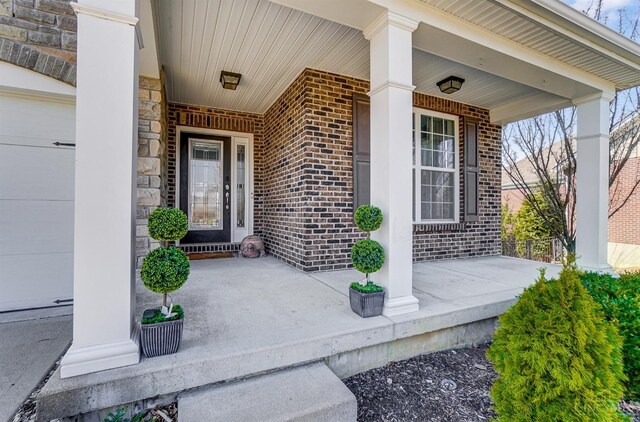 view of exterior entry featuring stone siding, brick siding, and covered porch