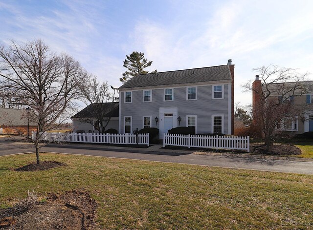 colonial inspired home featuring a front yard, a fenced front yard, and a chimney