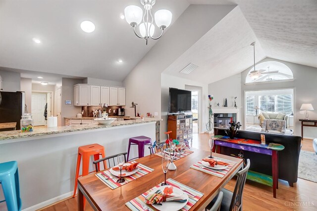 dining room featuring a chandelier, lofted ceiling, light wood-style flooring, recessed lighting, and a glass covered fireplace